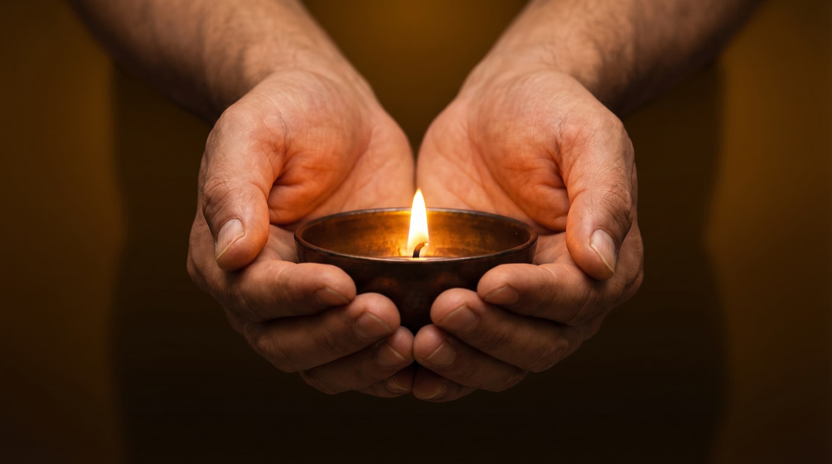 Two hands cupping a small oil lamp flame, evoking care and the protection of something fragile.