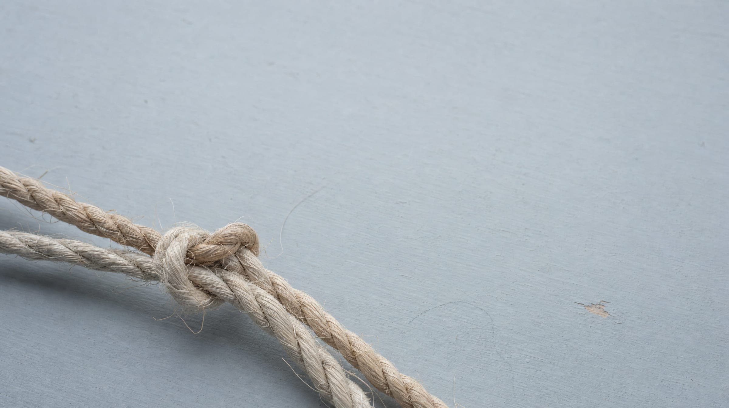 Undyed flax and hemp cords tied in a single knot on a pale blue-grey board, evoking the quipu, the Andean knotted-cord recording system from which the firm draws its name.